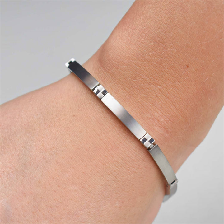 Een close-up van een pols met de Boccia Titanium Armband 0329-01. Het strakke, minimalistische ontwerp met een dunne, rechthoekige zilveren plaat is goed te zien.