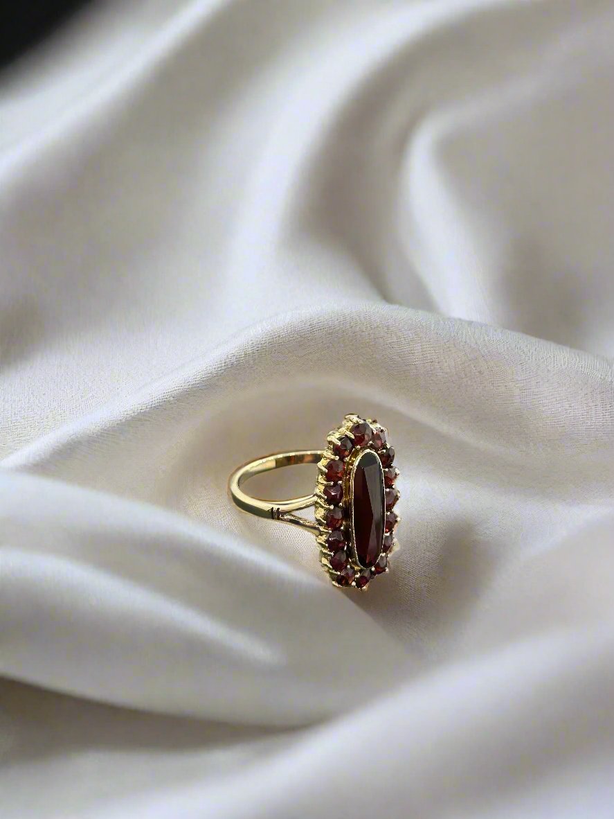 De vintage gouden ring 14k ovale granaat 3,7gr van Juwelier van der Kooij rust elegant op een witte, zijdeachtige stoffen achtergrond.