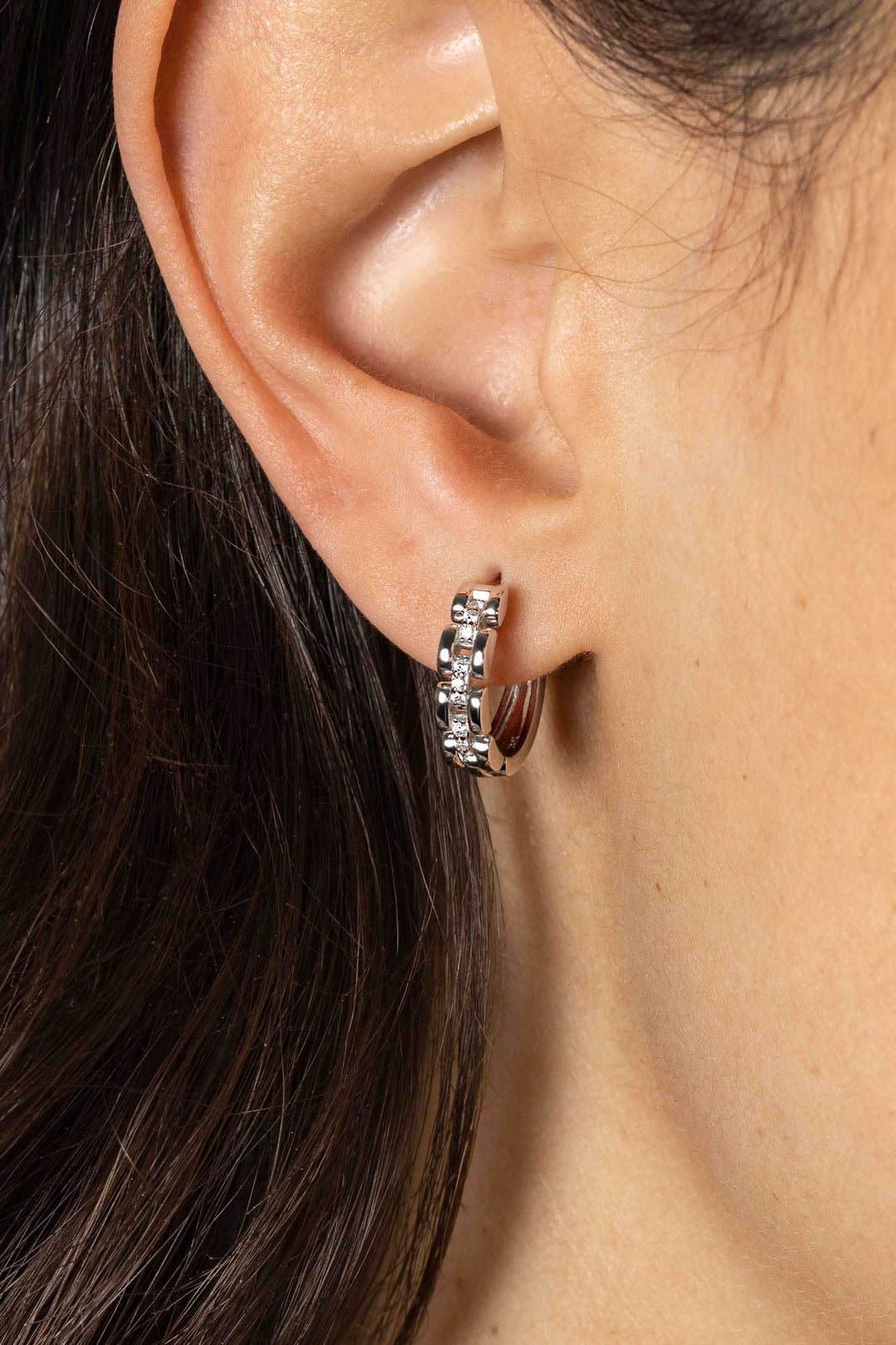 Close-up van het oor van een persoon die Zinzi Oorbellen Zilver Zio2504 met witte zirkonia draagt; donkerbruin haar verschijnt naast het oor.