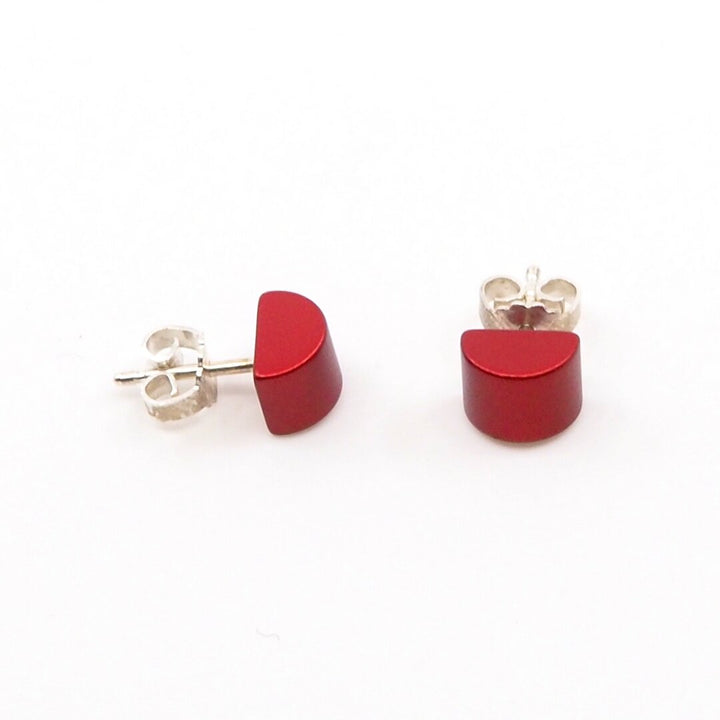 De Gekleurde half ronde oorbellen rood van Otra Cosa, vervaardigd uit geanodiseerd aluminium met zilveren paaltjes en vlinderruggen, worden weergegeven in een moderne stijl op een effen witte achtergrond.