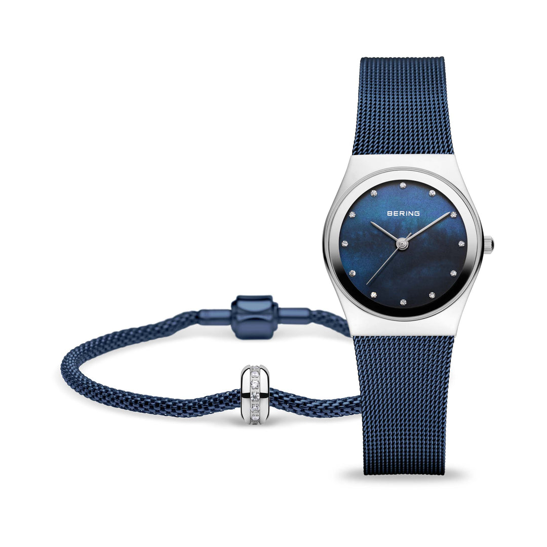De Bering 12927-307-GWP is een strak dameshorloge met een blauwe mesh band en donkerblauwe wijzerplaat, minimalistische uurmarkeringen, quartz uurwerk en een bijpassende armband met zilveren accenten. Dit alles elegant gepresenteerd tegen een witte achtergrond.