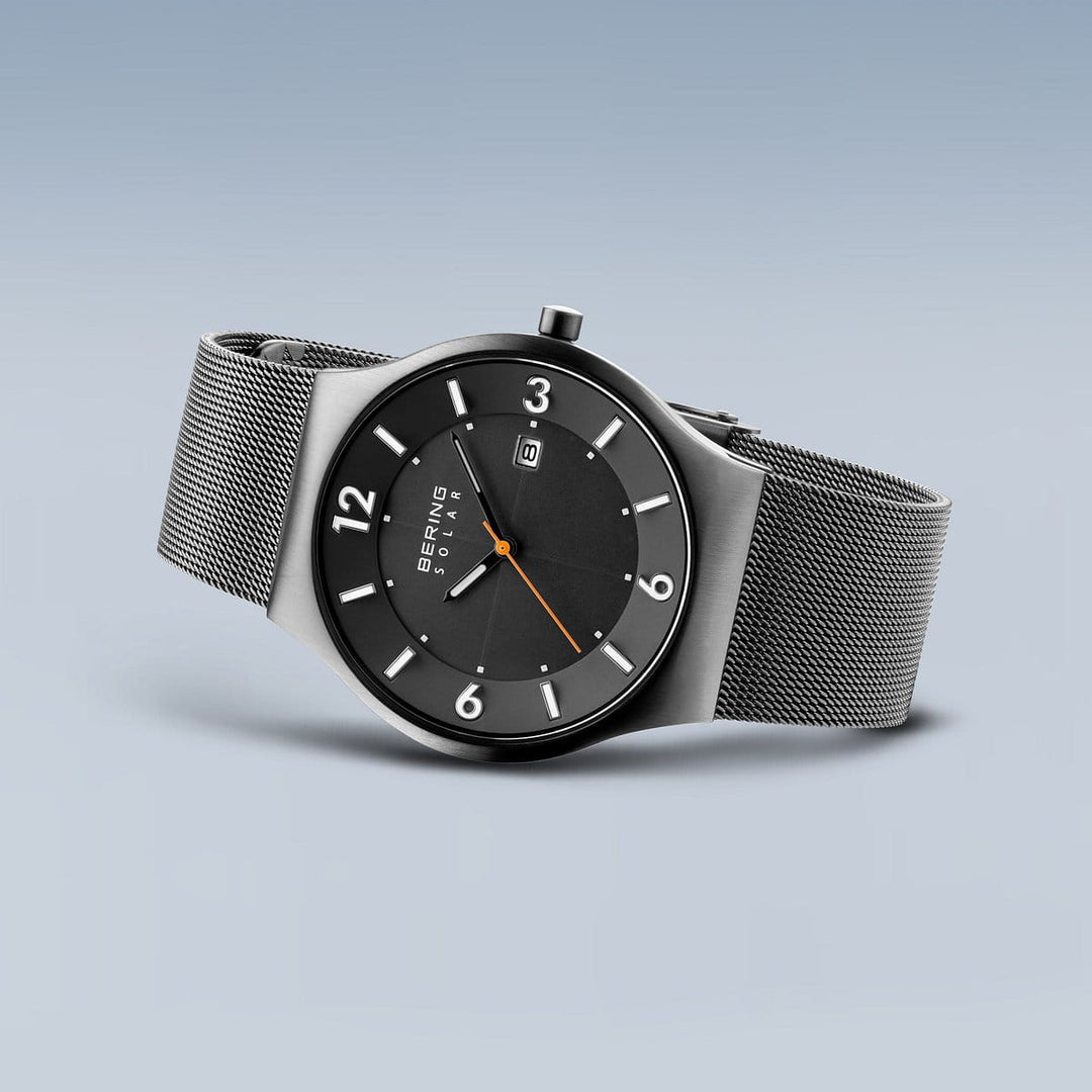 Het Bering 14440-077 Herenhorloge heeft een strak, modern design met Saffierglas. Het heeft een zwarte wijzerplaat, zilveren meshband, witte uurmarkeringen, een oranje secondewijzer en een minimalistische stijl. Er is ook een klein datumvenster op 12 uur op een lichtblauwe achtergrond met kleurverloop.