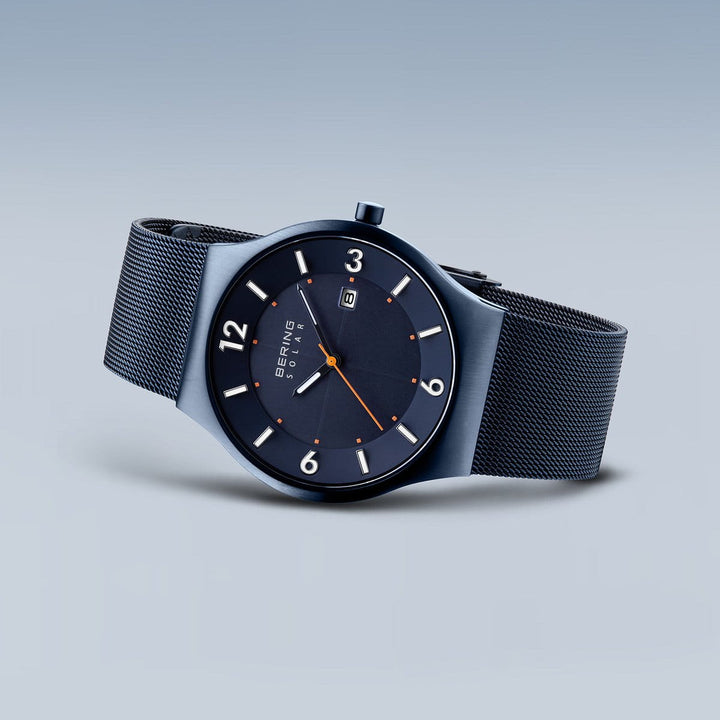 Het Bering 14440-393 horloge is voorzien van Saffierglas voor krasbestendigheid, een strak marineblauw ontwerp met een mesh band en een ronde wijzerplaat met grote witte cijfers, oranje minutenmarkeringen en een datumweergave op 6 uur. Het Solar-uurwerk mechanisme zorgt ervoor dat het tijdloze elegantie belichaamt.