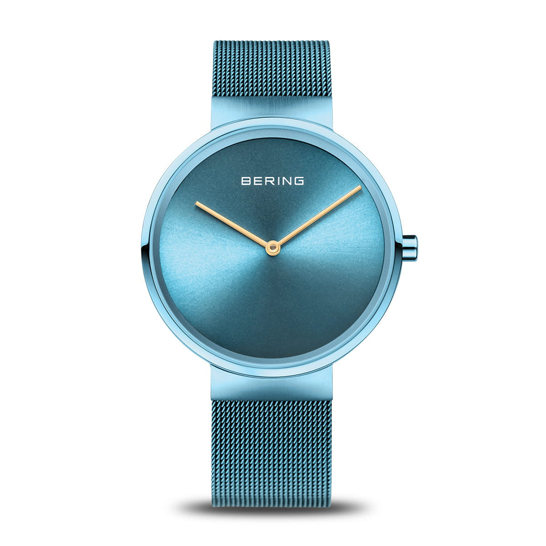 Het Bering dameshorloge 14539-388 heeft een minimalistisch design met een blauwe wijzerplaat, gouden wijzers, quartz-uurwerk, blauwe mesh-band en duurzaam saffierglas, dit alles elegant afgezet tegen een witte achtergrond.