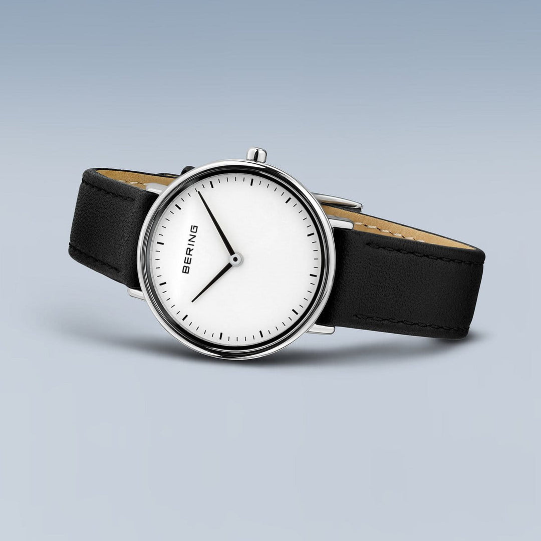Het Bering 15729-404 Dameshorloge heeft een blauwe achtergrond en straalt minimalistische elegantie uit met zijn witte wijzerplaat, dunne zwarte wijzers, zwarte leren band, strakke zilveren kast, Saffierglas en Quartz-uurwerk.
