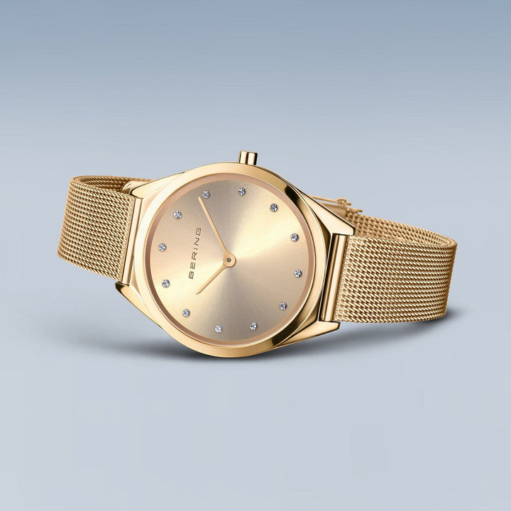 Het Bering 17031-333 dameshorloge heeft een minimalistisch goudkleurig design met een ronde wijzerplaat, diamantachtige uurmarkeringen, saffierglas en een meshband. Dit elegante horloge heeft een quartz uurwerk tegen een gradiënt blauwgrijze achtergrond.