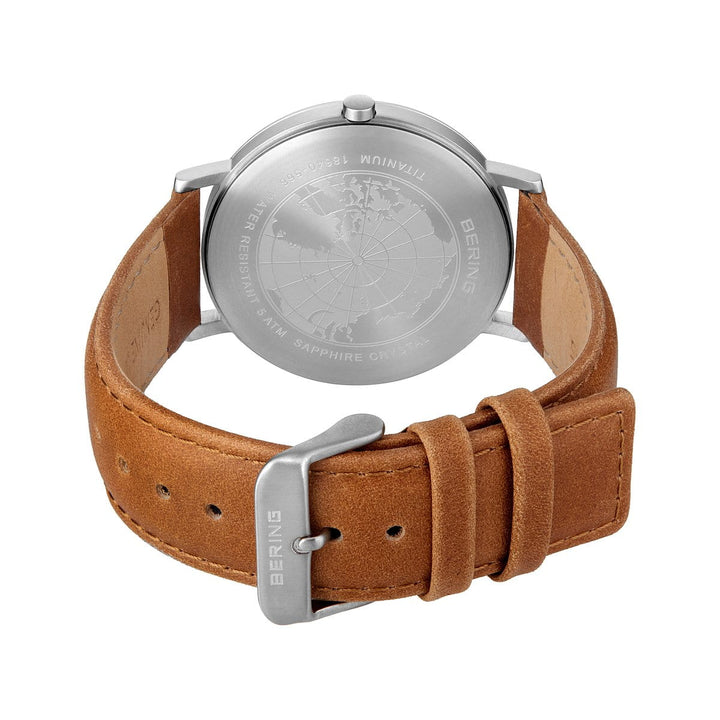 Het Bering heren horloge 18640-568 heeft een bruine leren band met zichtbare stiksels, zilveren gesp, titanium horlogekast met een gegraveerde wereldkaart en branding op de achterkant. Het heeft een groene saffierglas wijzerplaat en een zilveren afwerking voor extra elegantie.