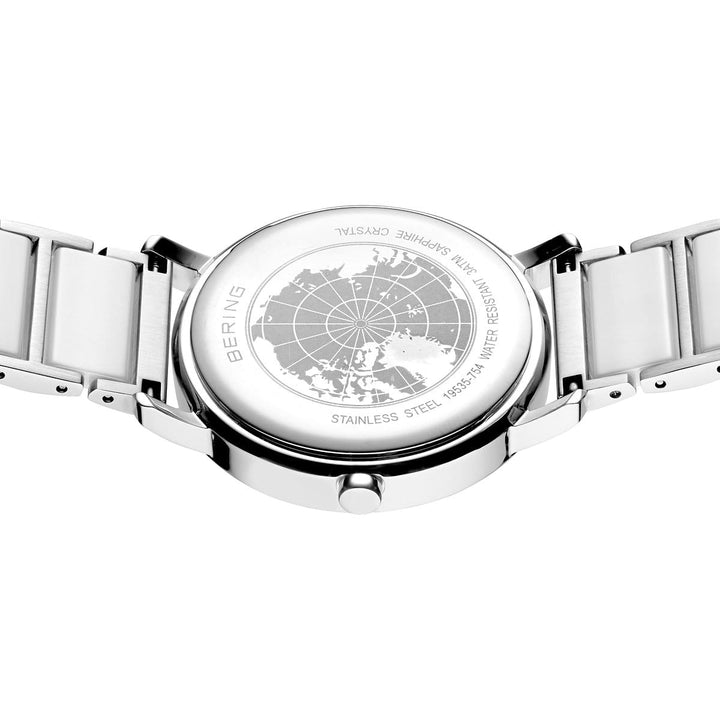 Het elegante Bering dameshorloge 19535-754 heeft een zilveren achterkant met een gegraveerde kaart en opschriften BERING, Stainless Steel, 316L, Sapphire Crystal, genummerd 15531-754, voorzien van een zilverkleurige keramische band en geavanceerde zonnetechnologie voor stijlvolle efficiëntie.