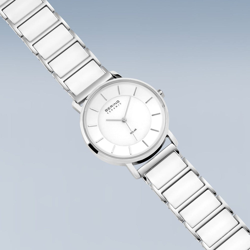 Het Bering dameshorloge 19535-754 heeft een strakke zilveren afwerking, een minimalistische witte wijzerplaat met eenvoudige uurmarkeringen en slanke wijzers, aangevuld met een zilverkleurige keramische band. Elegant gepresenteerd tegen een lichtblauwe achtergrond met kleurverloop, wordt het aangestuurd door zonnetechnologie.