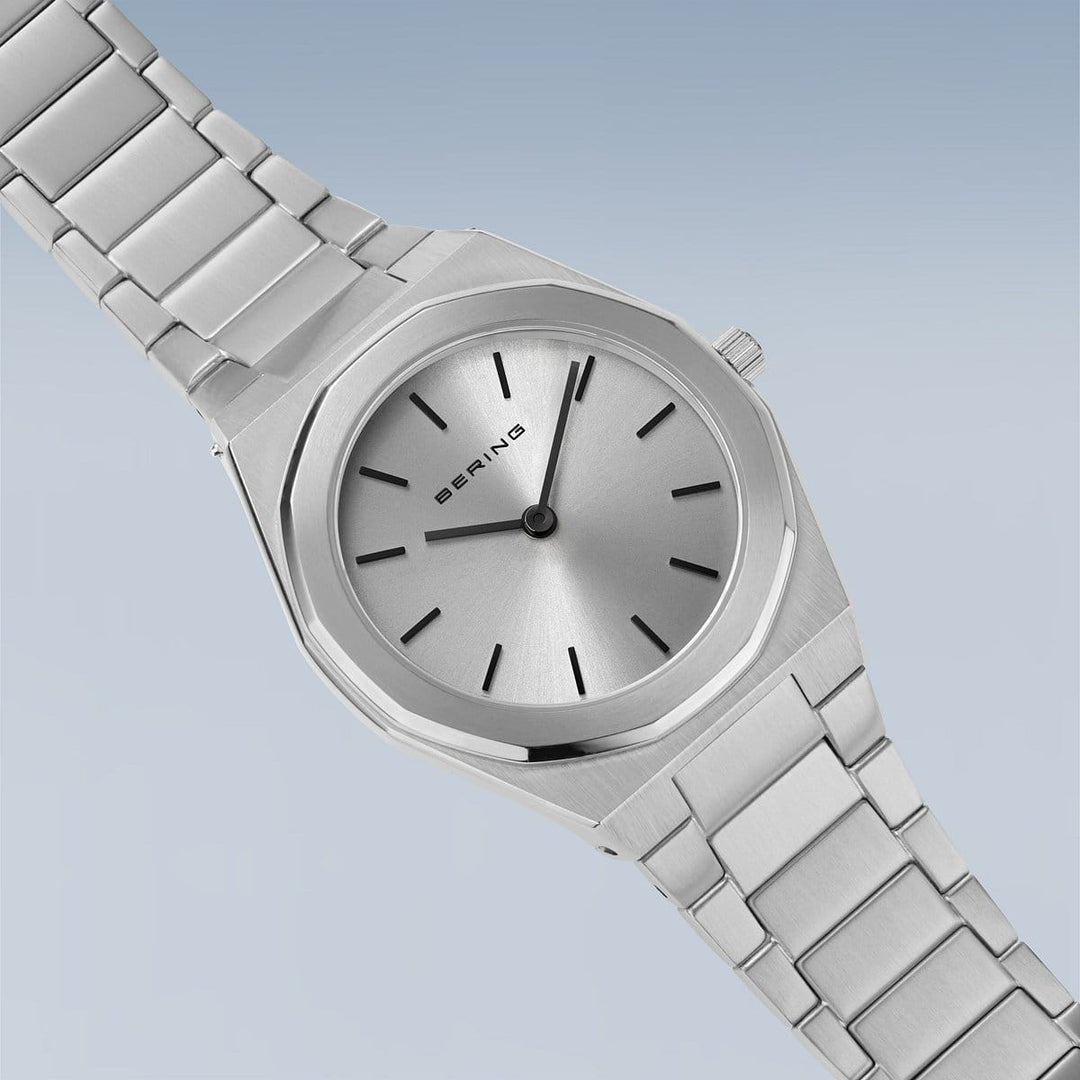Een minimalistisch Bering dameshorloge 19632-700 horloge, met saffierglas en een zilveren wijzerplaat met dunne zwarte markeringen en wijzers, staat elegant tegen een lichtblauwe achtergrond.