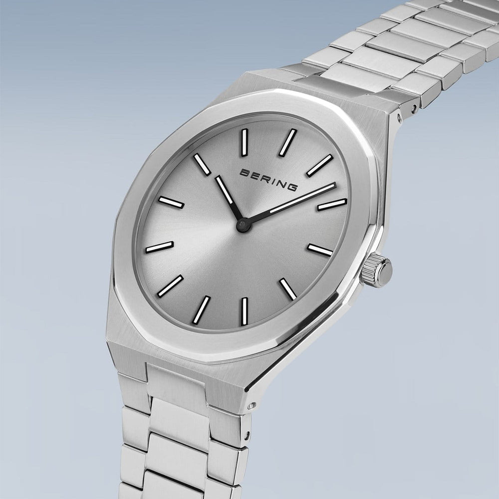 Het Bering herenhorloge, productnaam 19641-700, heeft een minimalistisch ontwerp met een zilveren wijzerplaat, ronde wijzerplaat, quartz-uurwerk, eenvoudige uurmarkeringen en een metalen schakelband tegen een lichtblauwe achtergrond.
