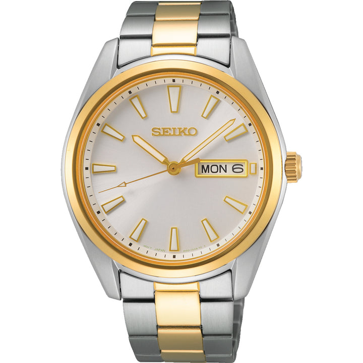 Het Seiko heren horloge SUR446P1 heeft een zilveren en gouden metalen band met een ronde wijzerplaat, gouden uurmarkeringen en wijzers. Het heeft een dag-/datumweergave aan de rechterkant, een gouden lunette en duurzaam saffierglas, wat elegantie en duurzaamheid combineert.