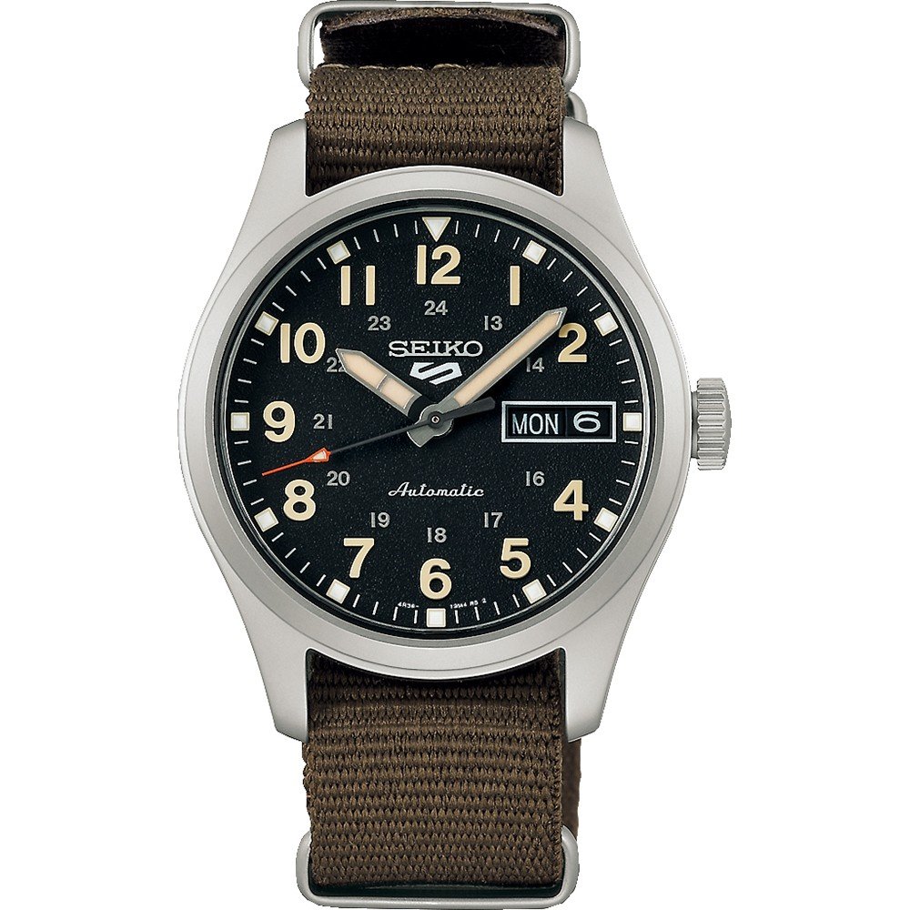Het Seiko 5 Sports herenhorloge SRPJ85K1 van Seiko heeft een zwarte wijzerplaat, een bruine stoffen band, een zilveren lunette, lichtgevende wijzers en cijfers, een dag-datumaanduiding op 3 uur en heeft zowel een 12-uurs- als een 24-uursmarkering.