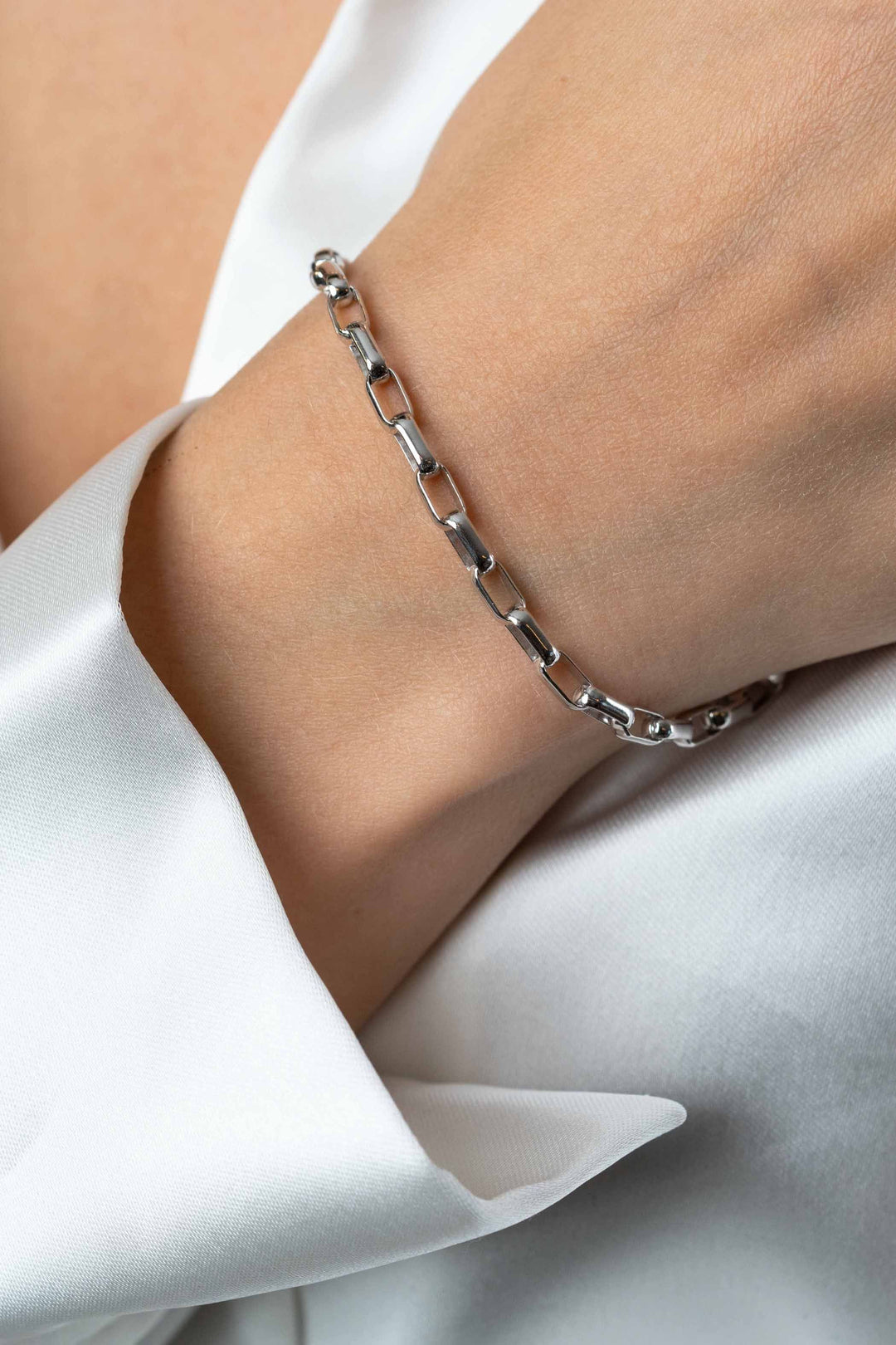 Een close-up van een pols met de Zinzi Armband zilver ZIA2514, deels bedekt door een witte satijnen mouw.