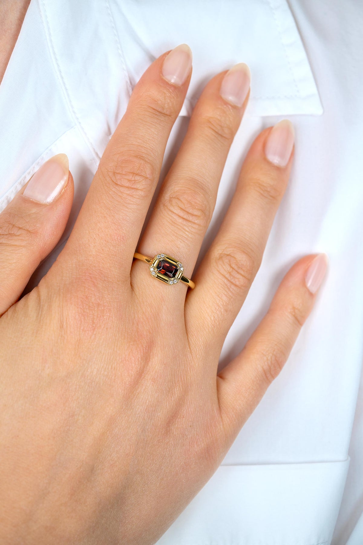 Bague en argent doré avec une pierre centrale colorée, portée sur un doigt.
