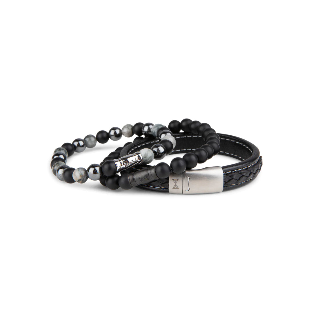 De AZE Jewels Kralen armband heren - Black Elk Peak set bestaat uit een stijlvolle kralenarmband met zwarte en grijze gemarmerde stenen en een zwarte gevlochten leren armband met een metalen sluiting.