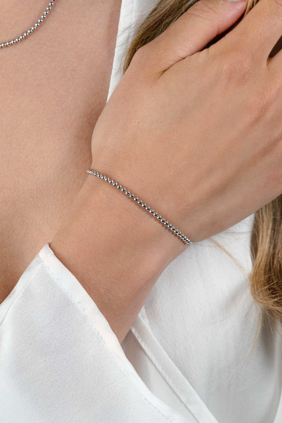 Een close-up van een pols versierd met de Zinzi armband Zilver ZIA2640, met elegante zilveren schakels. De drager, gekleed in een wit topje met lange mouwen, raakt zachtjes zijn nek aan.