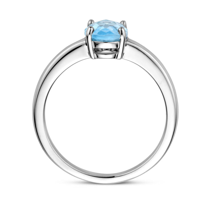 Een Van der Kooij Collectie ring blauw topaas zilver gerhodineerd met ronde, gefacetteerde blauwe topaas in een vierpoots zetting, zijaanzicht op witte achtergrond.