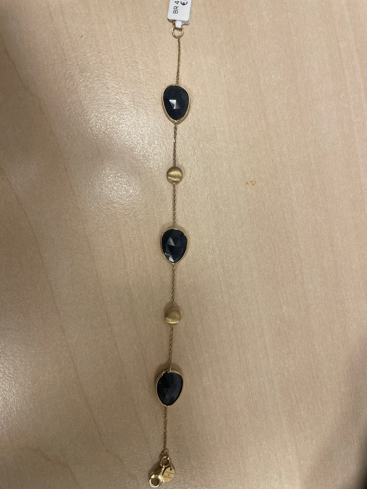 Bracelet doré avec des pierres noires et des détails dorés.