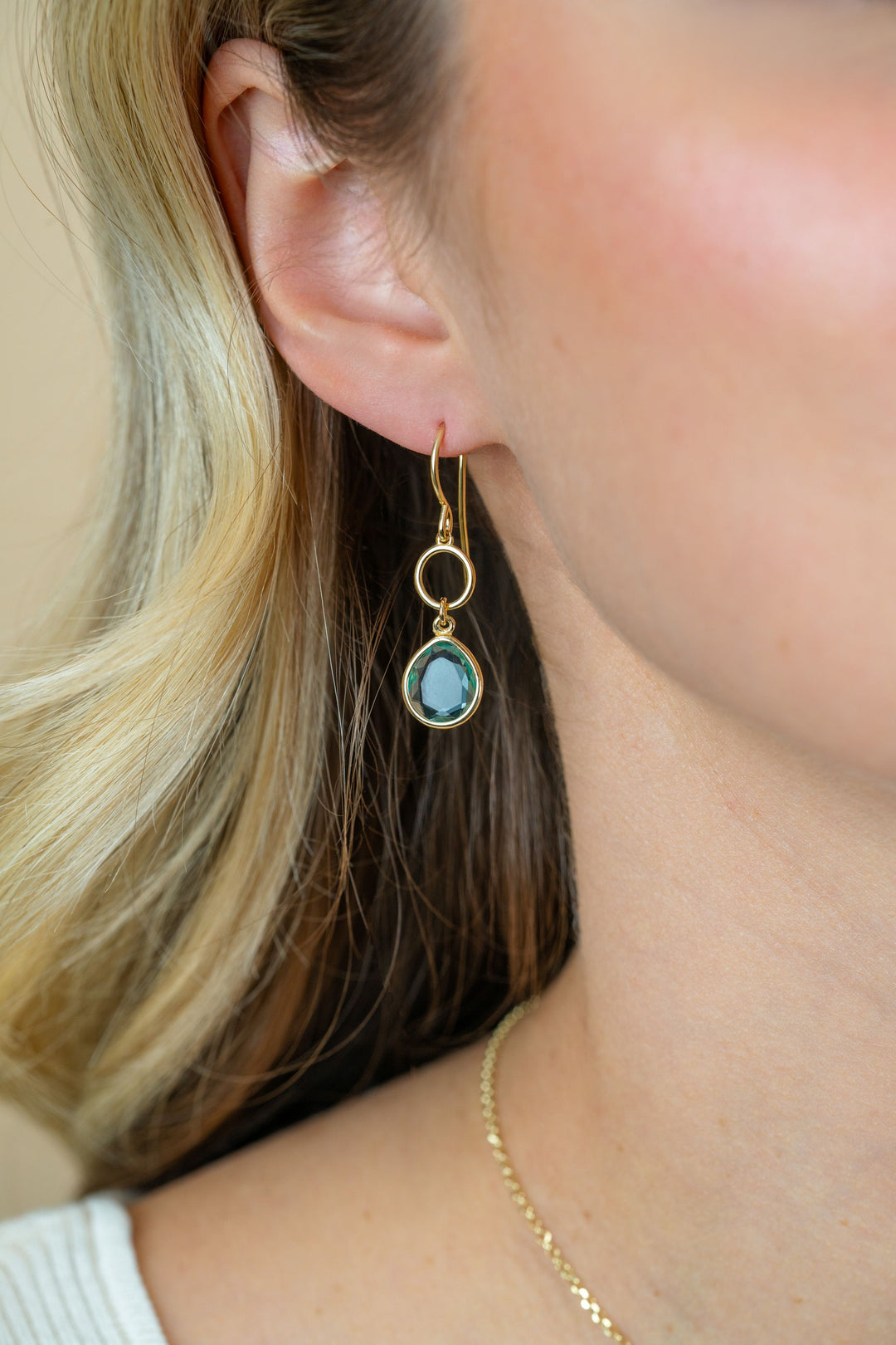 Close-up van een vrouwenoor met een Zinzi oorbellen vergulde ZIO2716G met een ronde turkooizen hanger. Ze heeft lichtblond haar, een gouden ketting en een zacht verlichte huid.