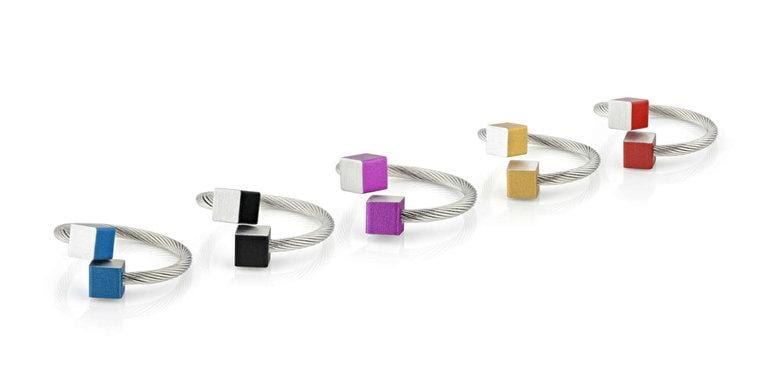 De CLIC Creations Ring Kubusjes Oranje R4O heeft vijf zilveren draadringen, elk eindigend in twee kleine kubussen, verkrijgbaar in blauw, zwart, paars, geel en rood met een metallic zilveren bijbehorende kubus. Ideaal voor degenen die van aanpasbare accessoires houden.