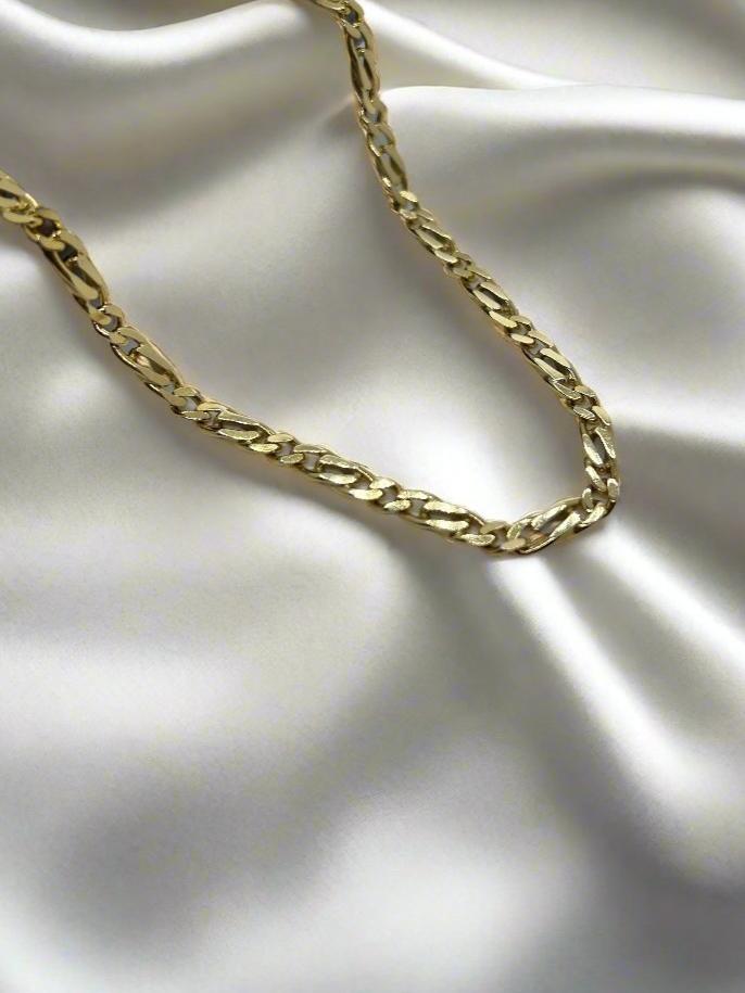 De vintage gouden collier 14K gourmette plat van Juwelier van der Kooij rust elegant op gladde, vloeiende witte zijden stof, waardoor een luxueus contrast ontstaat dat doet denken aan de Vintage Collectie sieraden.