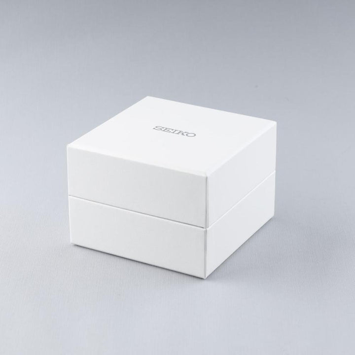 Een witte vierkante doos met Seiko erop, tegen een lichtgrijze achtergrond. Het heeft strakke lijnen en een matte afwerking, en belichaamt de tijdloze verfijning van het Seiko dameshorloge SWR072P1 met quartz uurwerkprecisie.