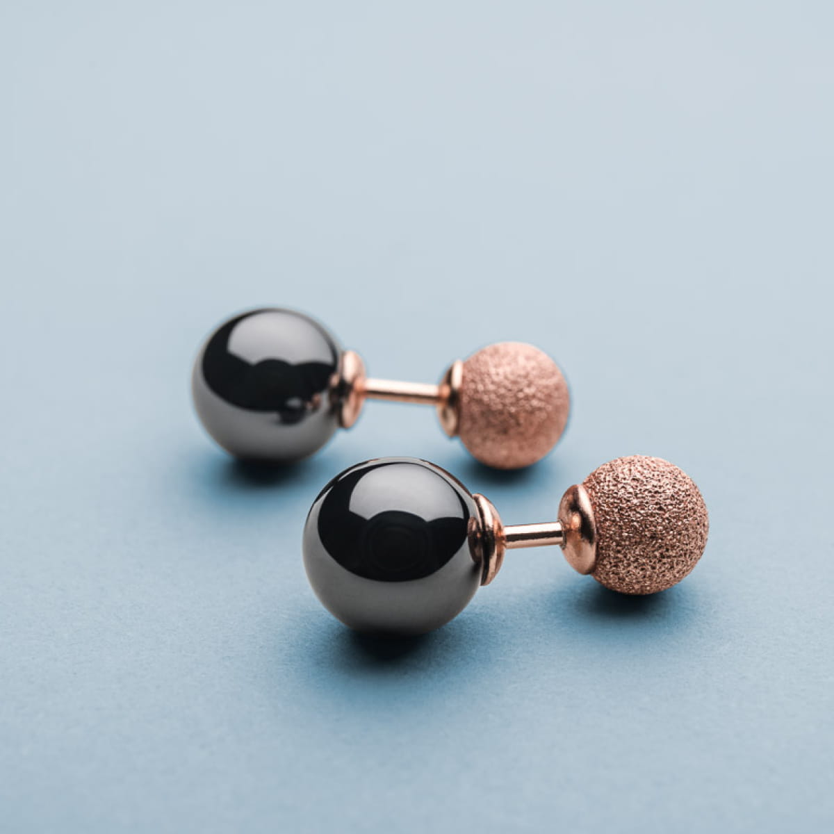 Boucles d'oreilles en métal rose avec perles noires brillantes et finitions texturées.