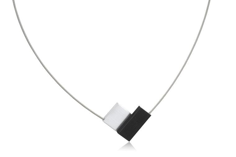 Collier en forme de V avec un pendentif noir et blanc, sur un cordon argenté.