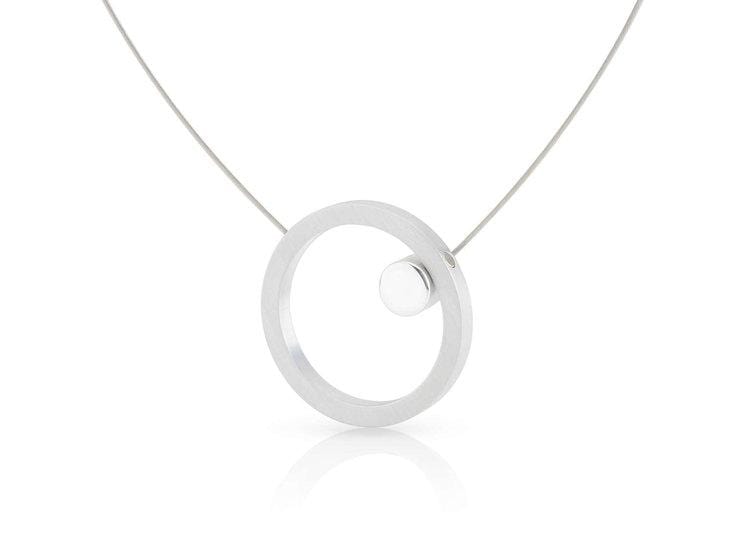 De Collier Grote ring met glans rondje C180 van CLIC Creations is een moderne, minimalistische ketting met een zilveren ronde hanger met een klein bolletje, opgehangen aan een delicate ketting. Handgemaakt in Nederland, het reflecteert subtiel licht en biedt een uniek maar eenvoudig ontwerp.