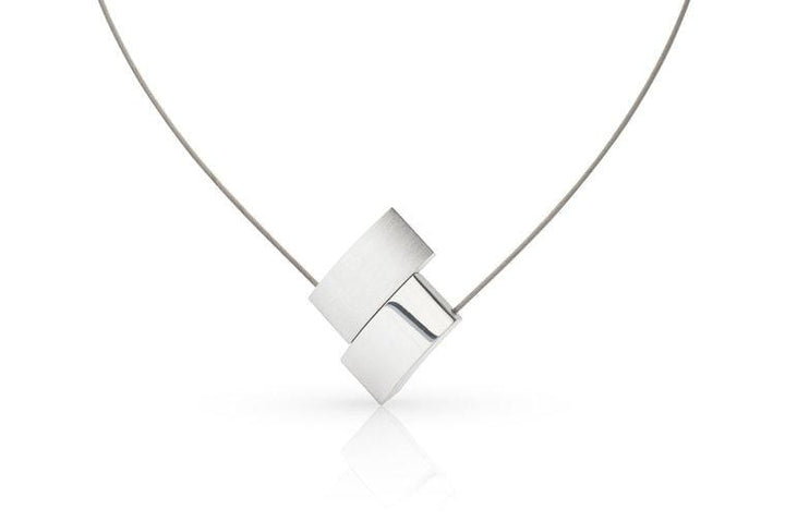 De Collier V-vorm C201 van CLIC Creations is een minimalistische zilveren ketting met twee in elkaar grijpende rechthoekige hangers aan een dunne draadketting. Handgemaakt in Nederland, het unieke ontwerp steekt elegant af tegen een effen witte achtergrond.