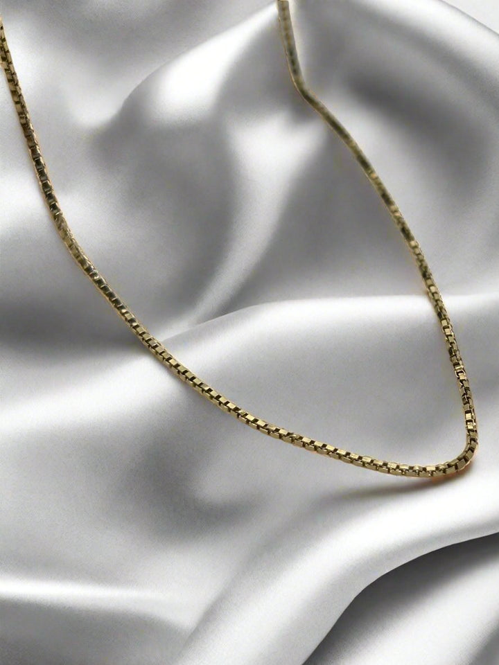 Het vintage gouden collier 45cm 14K venetiaans 3.2gr van Juwelier van der Kooij versterkt de gladde, witte satijn met een zacht, elegant contrast tussen het glanzende goud en de zijdezachte stof.