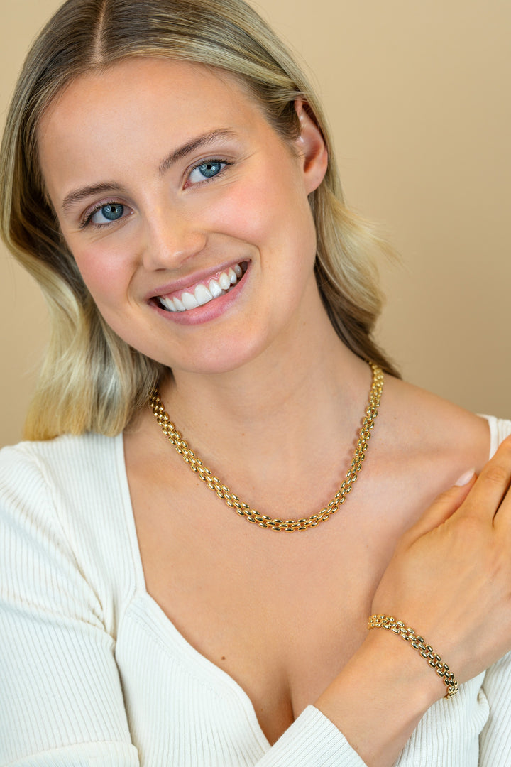 Een lachende blonde vrouw in een wit topje modelleert de Zinzi Armband Gold Plated ZIA2764G tegen een beige achtergrond.