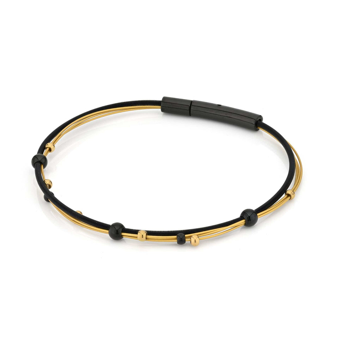 De Armband speelse bolletjes zwart bicolor A269ZG van CLIC Creations heeft een minimalistisch ontwerp met verweven zwarte en gouden strengen, geaccentueerd door kleine kralen. Gemaakt van chirurgisch edelstaal voor duurzaamheid, het bevat een strakke zwarte bajonetsluiting sluiting voor veilig dragen.