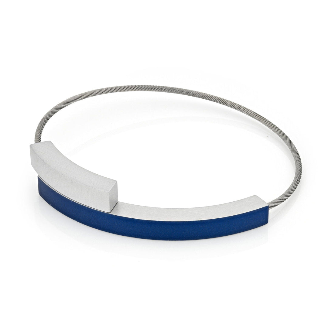 De Armband Twee boogjes Blauw A34B van CLIC Creations is een minimalistisch modern stuk met een flexibele zilveren kabel en twee gebogen rechthoekige metalen hangers, een mat zilver en de andere mat blauw, tegenover elkaar geplaatst. Deze handgemaakte armband heeft een magnetische sluiting voor naadloos dragen.