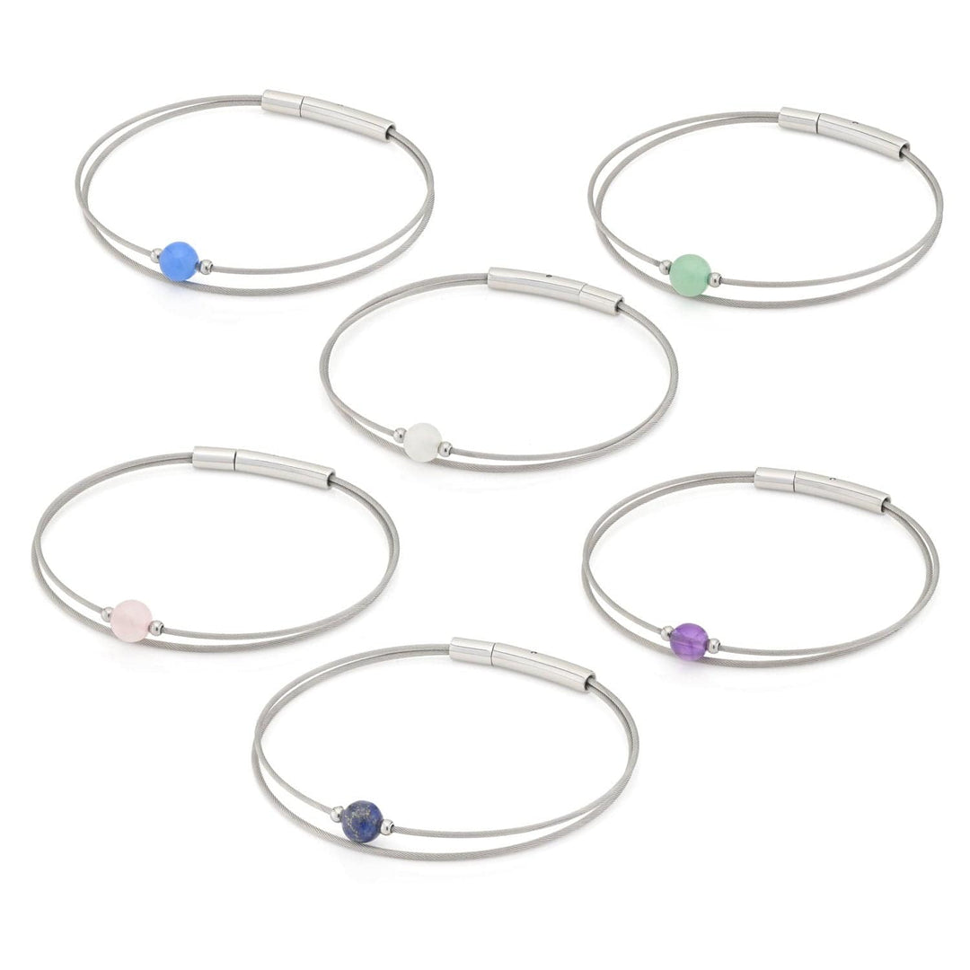 De Thinking of You-Armband Amethist A712B van CLIC Creations bestaat uit zes zilveren armbanden van roestvrij staal, elk met een andere centrale ronde kraal in de kleuren blauw, blauwgroen, wit, lichtroze, donkerblauw en amethist op dunne metalen bandjes.