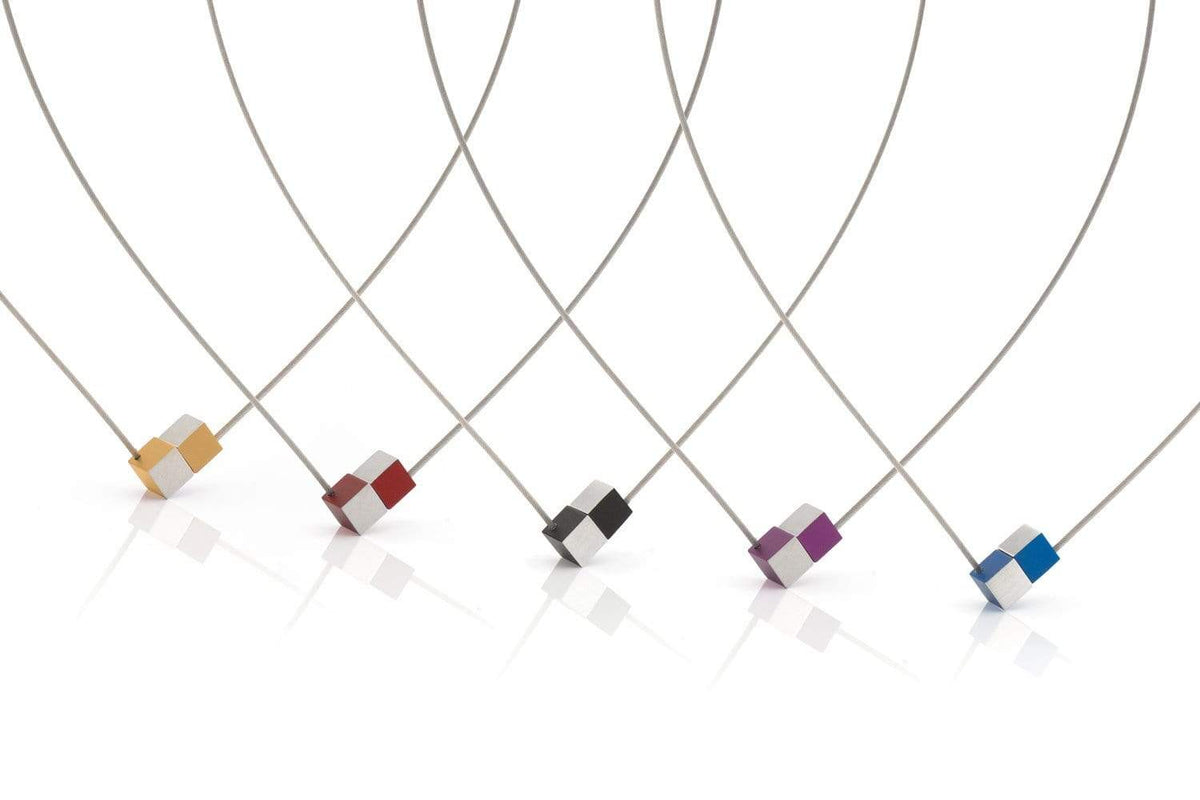 Afbeelding van vijf minimalistische kettingen van CLIC Creations, met de Collier Twee kubusjes Blauw C205B met edelstalen collier draad en tweekleurige kubushangers in verschillende tinten: oranjegeel, roodgrijs, zwartzilver, paarsblauw en roodblauw. Elk heeft een uniek ontwerp met een elegante magnetische sluiting.