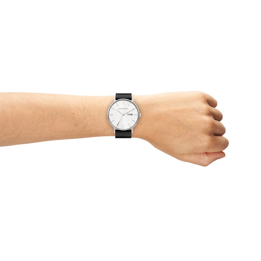Een close-up van de onderarm van een persoon met gebalde hand waarop de Jacob Jensen 160 te zien is, een minimalistisch quartzhorloge met een ronde zilveren wijzerplaat, een zwarte leren band, duurzaam saffierglas, minimale markeringen en een slank design.