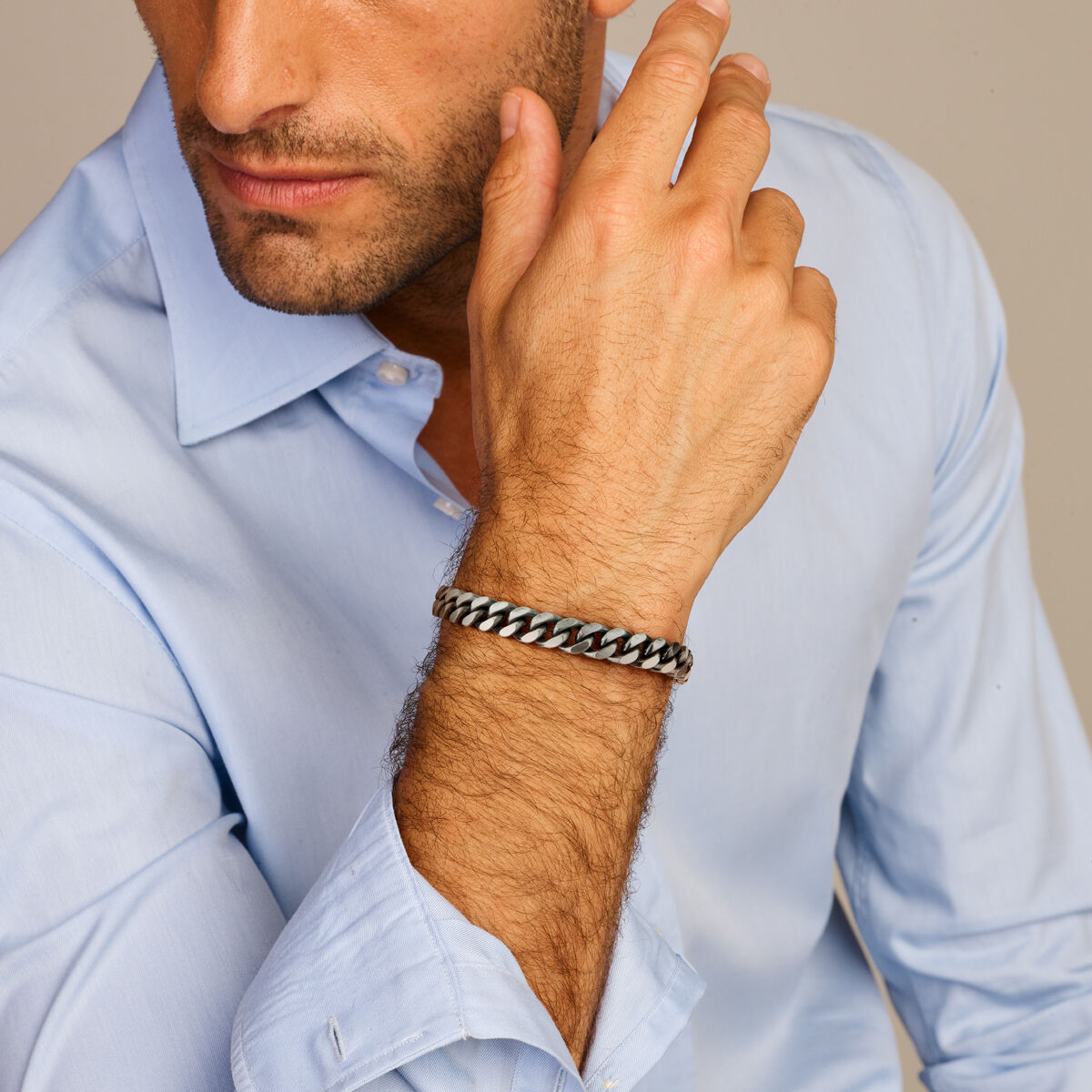 Een man in een lichtblauw overhemd laat zijn kin op zijn hand rusten en toont een Van der Kooij Collectie armband oxi gourmette 6-zijdes geslepen 8,5 mm zilver geoxideerd. Alleen de onderste helft van zijn gezicht en bovenlichaam zijn zichtbaar.