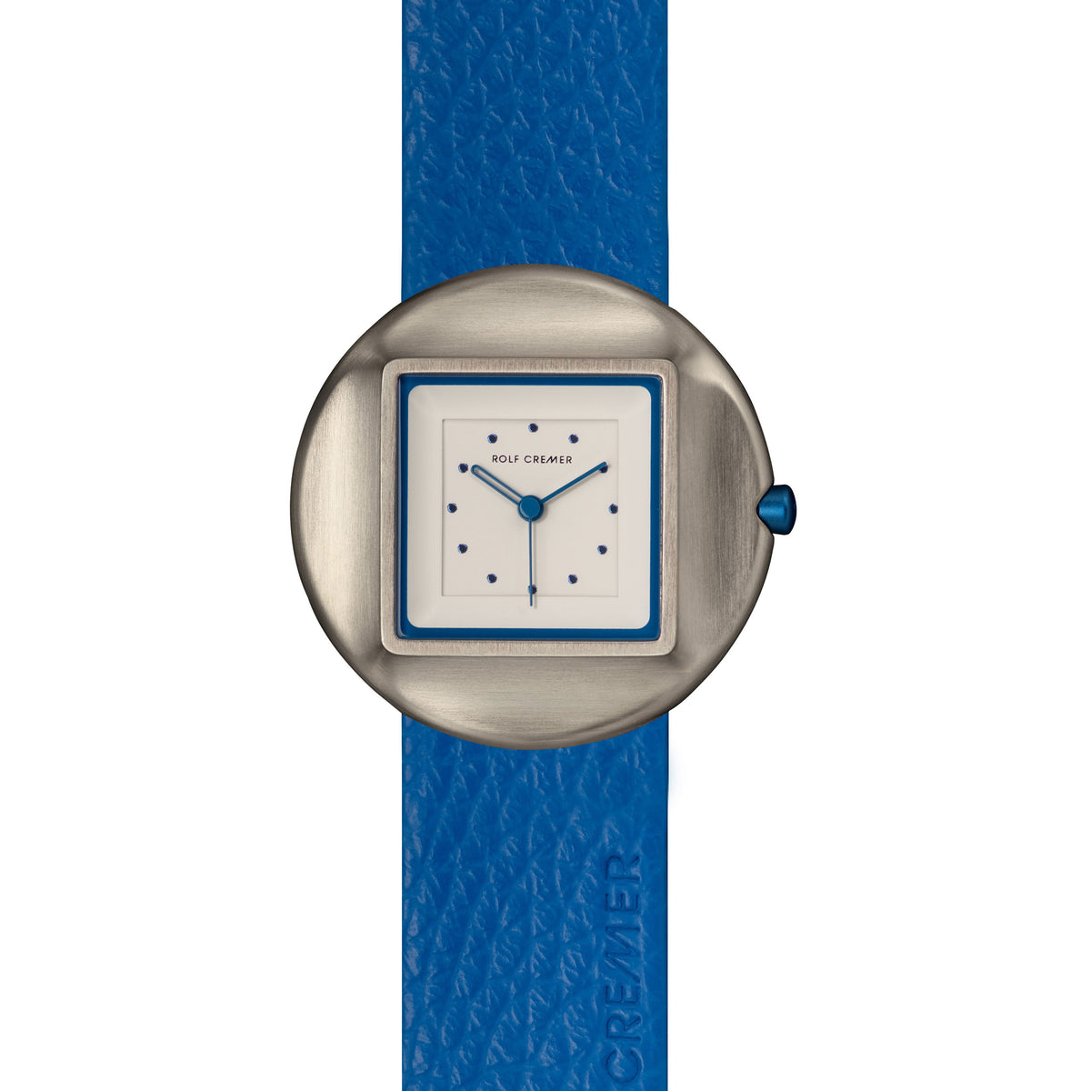 Montre Rolf Cremer avec un boîtier argenté, cadran carré blanc et bracelet en cuir bleu.