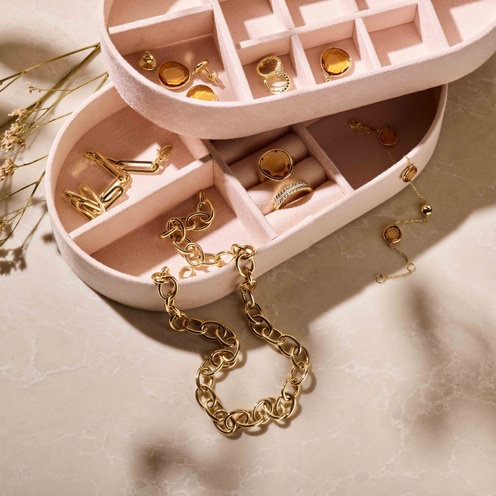 Twee Van der Kooij Collectie sieradenbox zachtroze toebehoren met vakjes bevatten gouden ringen, oorbellen en manchetknopen. Op het beige marmer liggen een grove goudkleurige en een fijne armband-stijlvol voor dames.