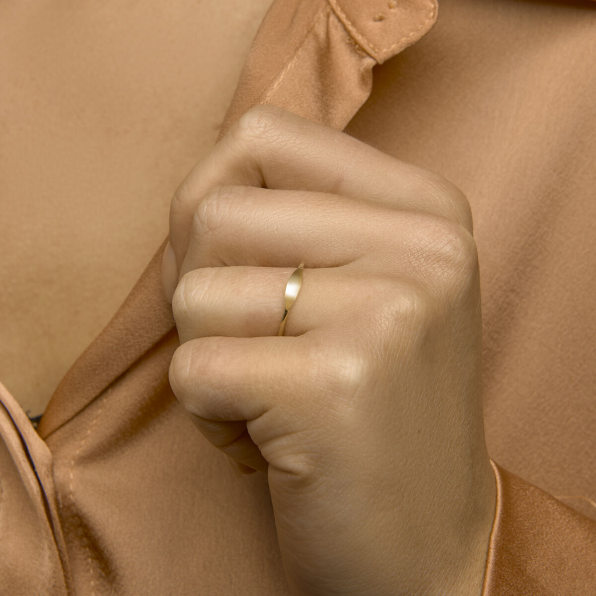Een close-up van een lichtbruine hand die de Van der Kooij Collectie graveerring 14K geelgoud om de ringvinger draagt, tegen de achtergrond van een lichtbruine satijnen blouse.