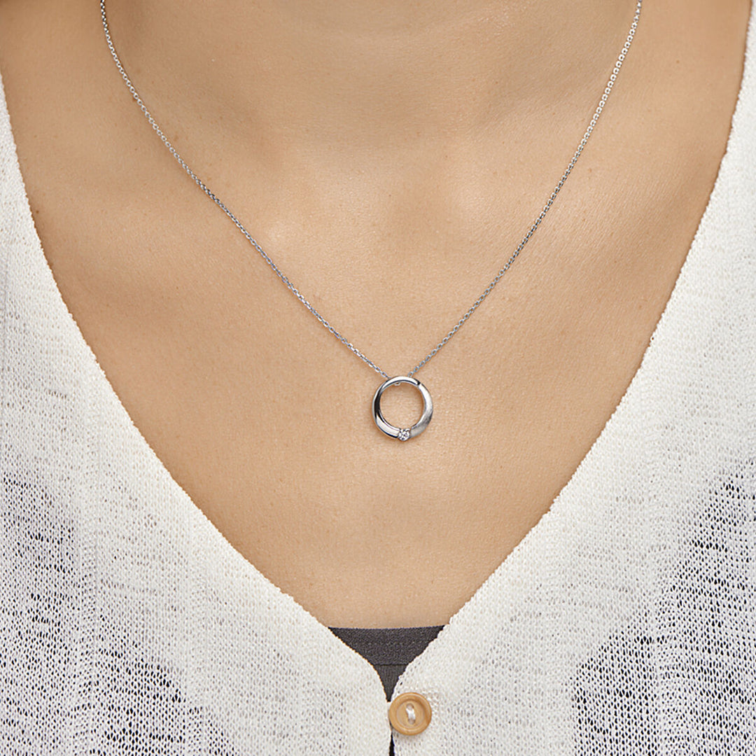 Een close-up van een vrouw met de Van der Kooij Collectie hanger rond zirkonia poli/mat zilver gerhodineerd, voorzien van een ronde hanger met een kleine zirkonia. Ze is gekleed in een wit gebreid topje met één zichtbare knoop.