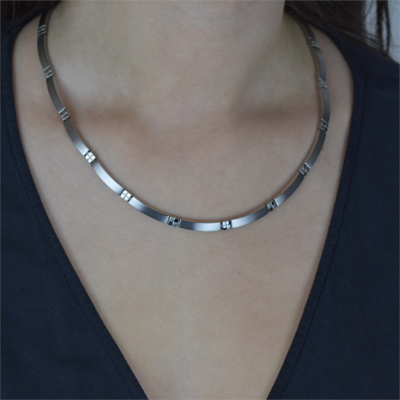 Een persoon draagt een donker topje met V-hals en een Boccia Titanium Collier 0831-01, een strakke Boccia-ketting met kleine rechthoekige accenten, gemaakt van duurzame materialen, om de nek.