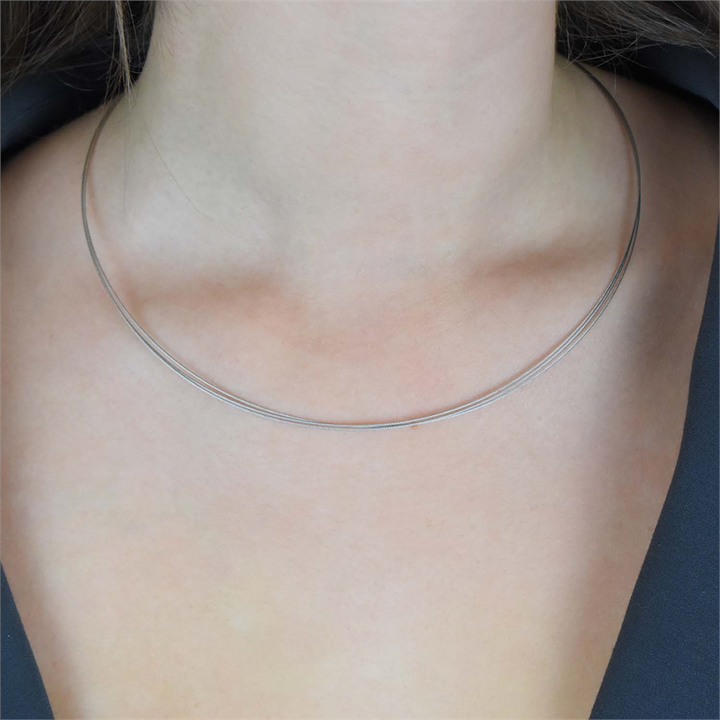 Een close-up van de nek van een persoon die de Boccia Titanium Lengte Collier staal 0804-01 van Boccia draagt, met een V-vormige opening aan de voorkant, afgebeeld tegen een donkere achtergrond.