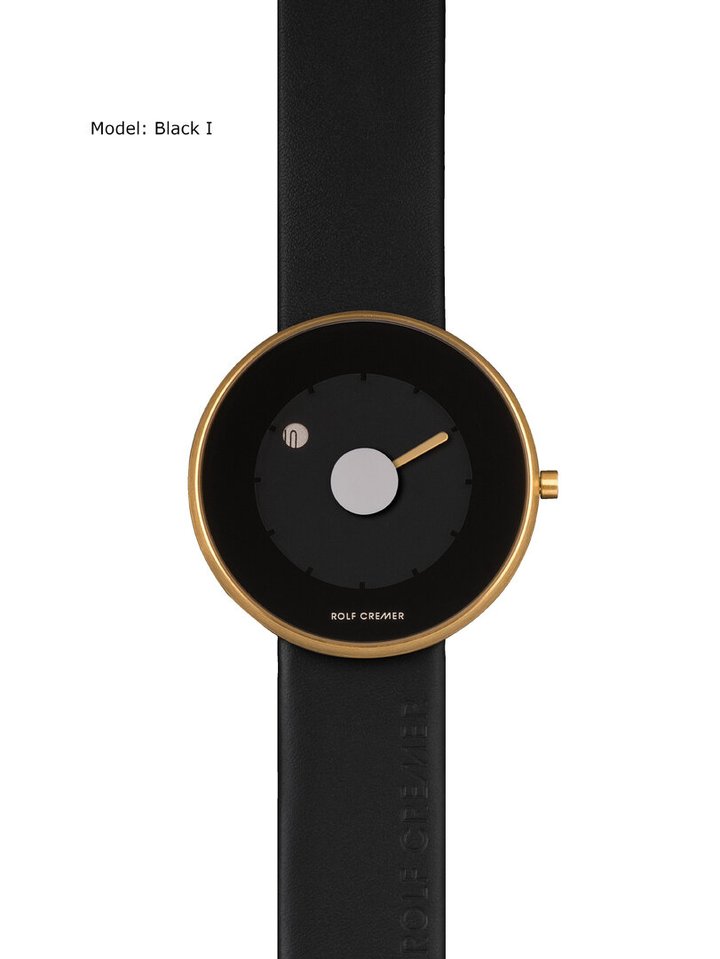 Montre Rolf Cremer avec un cadran noir et un boîtier doré, bracelet en cuir noir.