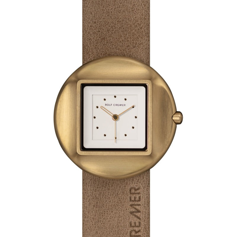 Montre Rolf Cremer avec boîtier rond en métal doré et cadran carré blanc, bracelet en cuir beige.
