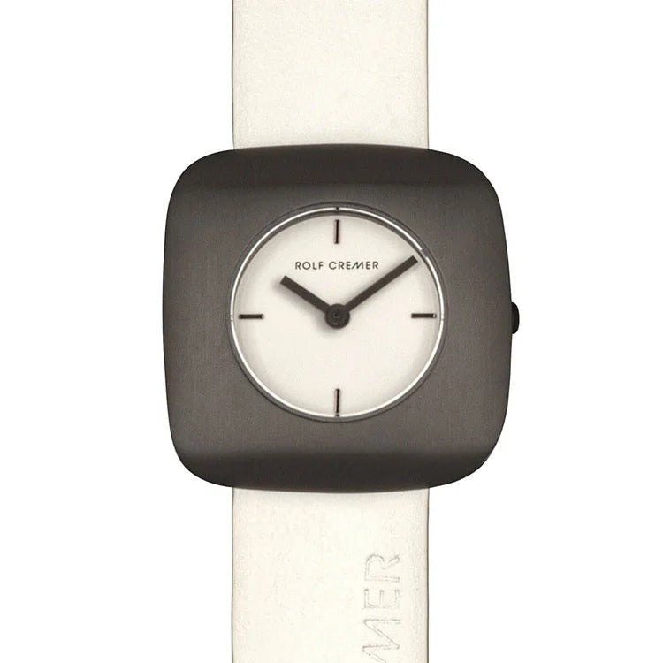 Montre Rolf Cremer avec boîtier carré noir, cadran blanc et bracelet en cuir beige.