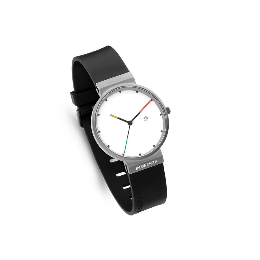 De Jacob Jensen 642 is een minimalistisch polshorloge met een strakke zwarte band, zilveren titanium kast en witte wijzerplaat. Het heeft rode, groene en gele wijzers met zwarte uurmarkeringen rond een centrale stip, aangestuurd door een nauwkeurig quartz uurwerk.