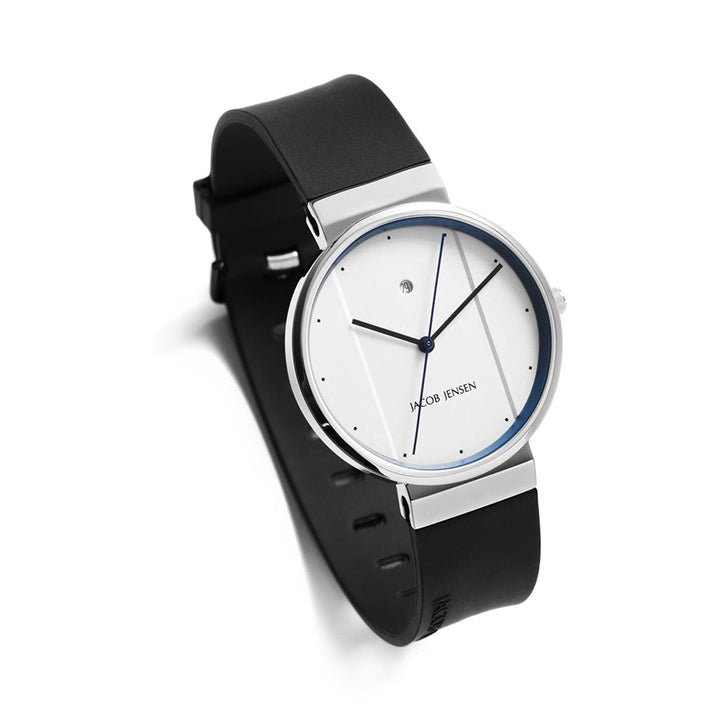 Het Jacob Jensen 750 horloge heeft een strak, minimalistisch design met een witte wijzerplaat, dunne blauwe wijzers en een kleine centrale wijzerplaat. De zwarte leren band past perfect bij de roestvrijstalen behuizing, allemaal aangestuurd door een quartz uurwerk voor moderne elegantie.